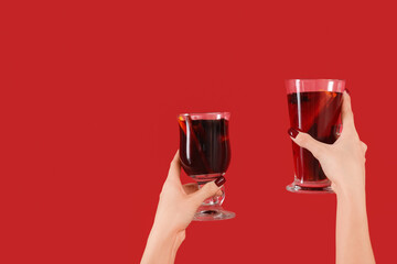 Female hands with glasses of warm mulled wine on red background