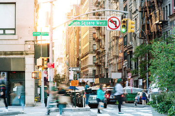 Crowds of people crossing a busy street corner at Union Square Park in New York City with sunlight background