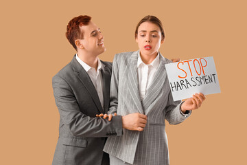 Business woman holding paper with text STOP HARASSMENT and her male colleague on beige background