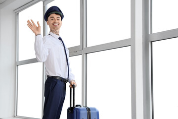 Male pilot with suitcase waving hand near window at airport © Pixel-Shot
