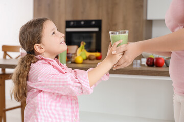 Mother giving little daughter glass of healthy smoothie in kitchen