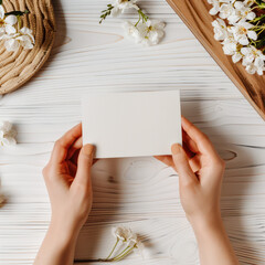 Obraz premium Close up of a Blank Paper Card Holded by Woman Hand on White Wood Table With Flower