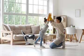 Young father and his daughter in rubber gloves giving high-five to each other at home