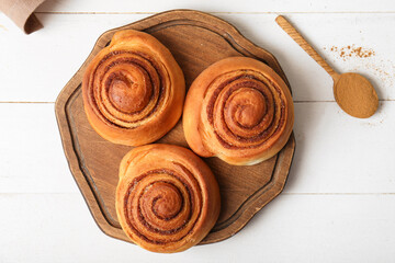 Board with sweet cinnamon rolls on white wooden background