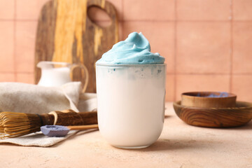 Glass of blue dalgona matcha latte, wooden bowls and chasen on table, closeup
