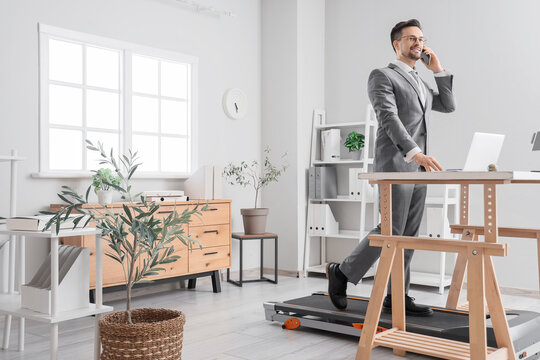 Handsome businessman talking by mobile phone on treadmill at table in office - Powered by Adobe