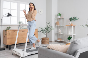 Young businesswoman talking by mobile phone on treadmill at home
