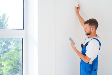 Male worker with tablet computer installing alarm system in room
