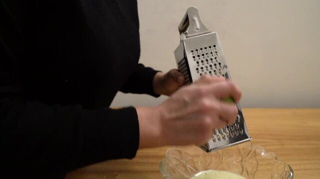 Bakery. Closeup view of a woman grating a lime with a metal rasper, into a bowl containing a citric cream.