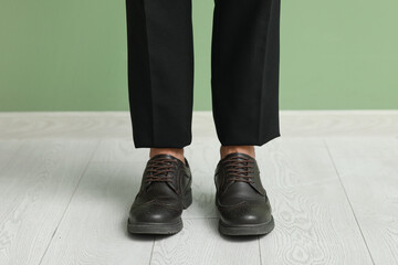 Stylish young businessman in elegant shoes near green wall, closeup