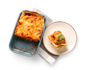 Baking dish and plate with tasty enchilada on white background