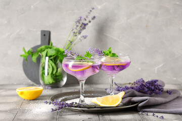 Glasses of fresh lavender lemonade with mint and flowers on grey tile table
