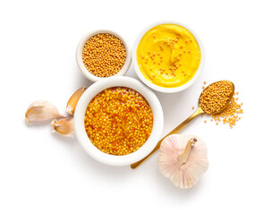Bowls of Dijon mustard with seeds and garlic on white background