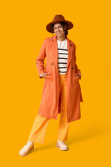 Beautiful young happy African-American woman in autumn outfit on orange background