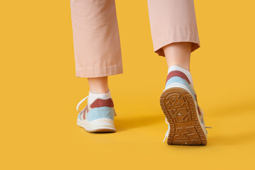 Female legs in sneakers on yellow background