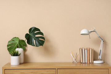 Wooden table with books, monstera leaves and desk lamp near beige wall © Pixel-Shot
