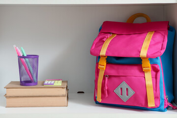 Shelf with books, school supplies and backpack, closeup
