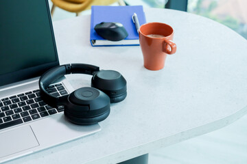 A black headphones on the laptop keyboard. A coffee cup and notebook in the background