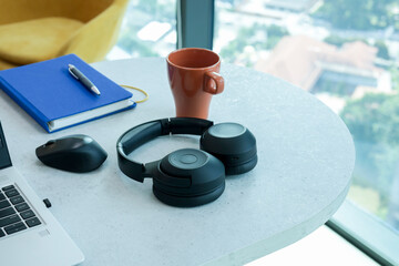 Headphones on the office table with a cup of coffee, notebook, and yellow couch in the background