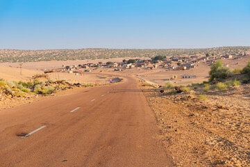 Empty high road or national high way approaching remote desert village inside the desert. Distant horizon, Hot summer at Thar desert, Rajasthan, India.