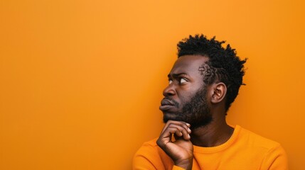 Puzzled African American man in orange top, lost in thought.