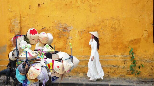 Asian woman wearing traditional Vietnamese culture walks beside an old wall in Hoi An, Vietnam.