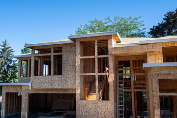 New large residential home construction in framing stage, with exterior walls covered in OSB sheathing, view from front of grand staircase and interior wood stud framing
