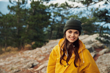 Smiling woman in yellow raincoat and hat enjoying the beauty of nature in the mountain landscape