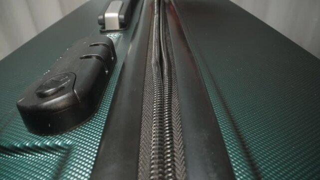 A Hand detaches the zipper pull from the lock on a suitcase, marking the moment before opening after a secure trip.