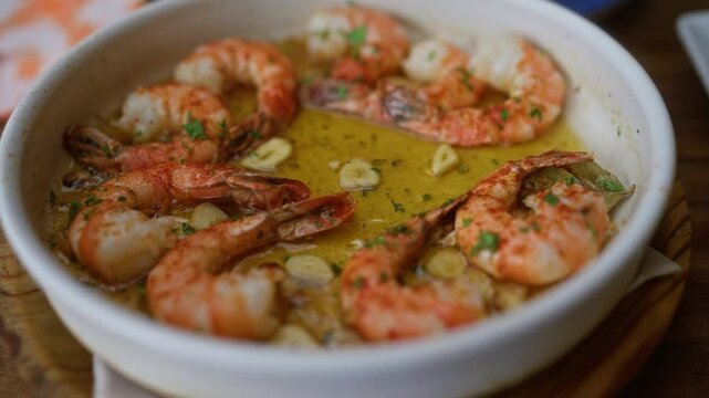 Grilled shrimp served in garlic butter with parsley garnish in a white bowl at a restaurant table shows the delicious detail of the seafood dish in a close up