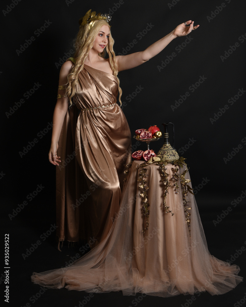 Poster Full length portrait of beautiful female model wearing gold grecian silk toga robes, historical fantasy goddess  persephone holding pomegranate fruit. Standing pose isolated studio background.