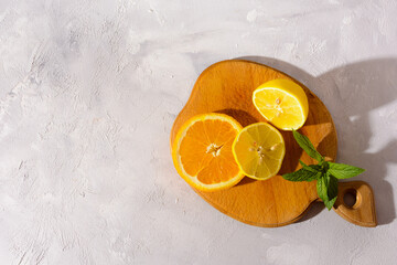 A close-up shot of a wooden cutting board with fresh lemon and orange slices. There are two lemons and one orange, all cut in half, on a gray background