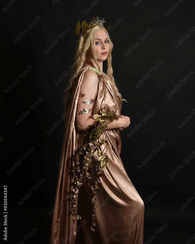 Canvas Prints Close up portrait of beautiful blonde female model wearing gold grecian silk toga robes and crown, historical fantasy goddess persephone holding pomegranate fruit. isolated on dark studio background.