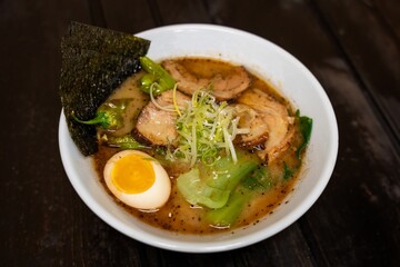A mouth-watering bowl of Kumamoto ramen topped with an egg, green vegetables, seaweed, and slices of meat, served in a savory broth, capturing a traditional Japanese meal.