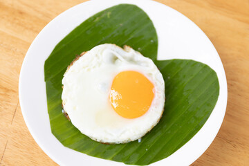 A freshly cooked egg on a white plate, presented with a banana leaf for a touch of natural elegance and simplicity.