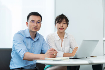 Two asian businesspeople working together in the office while using laptop