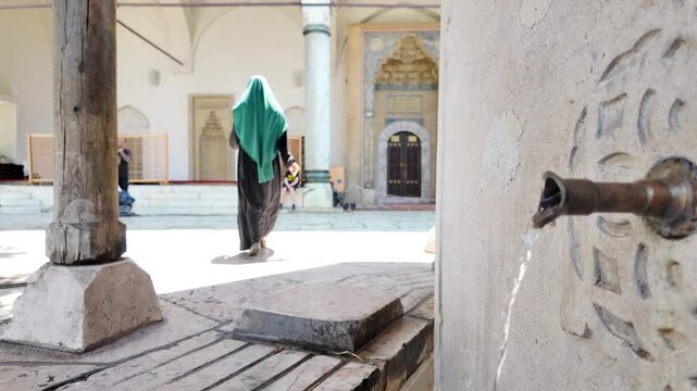 Woman with hijab walking in the courtyard of the Gazi Husrev Bey's Madrasa in Sarajevo, Bosnia Herzegovina. Slow motion.  Water flows from the fountain.