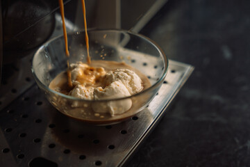 Coffee pouring from a coffee machine onto ice cream in a glass container.