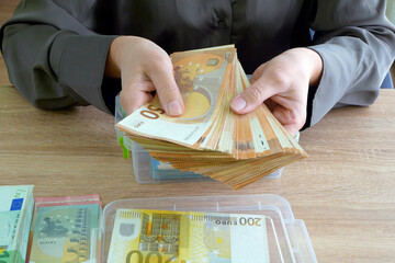 Unknown businesswoman sitting at the table and counting a lot of euro money
