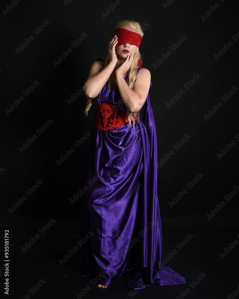 Poster Close up portrait of beautiful blonde female model wearing silk grecian toga dress and red blindfold, historical fantasy goddess,  isolated on dark studio background.