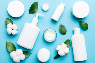 Organic cosmetic products with cotton flower and green leaves on color background. Flat lay