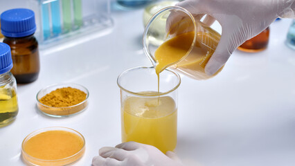 Lab theme photo for cosmetic advertising, which made from natural turmeric, was taken from close-up high angle on white table top. Researcher pouring yellow liquid from a beaker into other one