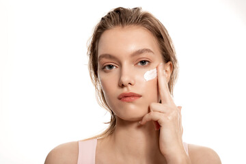 Fototapeta premium Blonde girl taking care of her skin and applying moisturizer cream to her face 