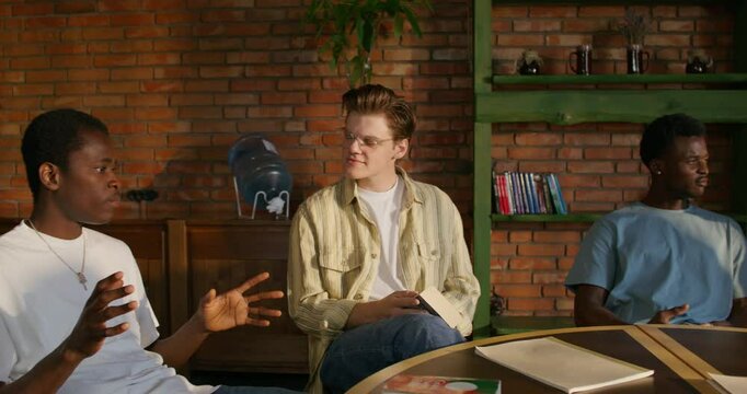 Bible Study Group. Young people talk in pairs while sitting at a table indoors. The books are on the table. Daylight