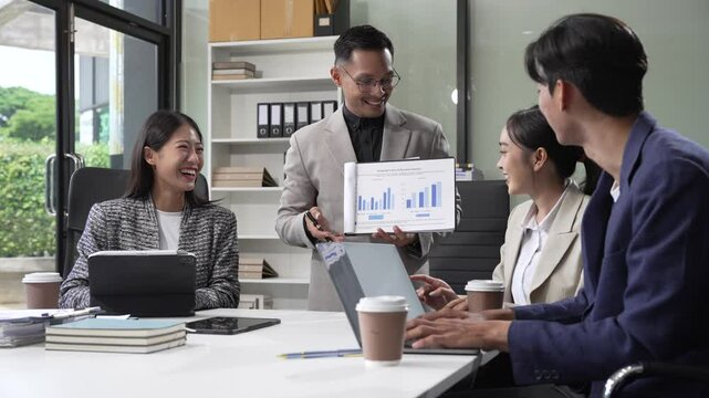 In an office, an Asian team meets at a desk, analyzing financial data on a monitor. They discuss business finance, operational guidelines, and strategies for success, data-driven decision-making.