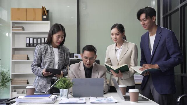 In an office, an Asian team meets at a desk, analyzing financial data on a monitor. They discuss business finance, operational guidelines, and strategies for success, data-driven decision-making.