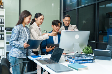 In an office, an Asian team meets at a desk, analyzing financial data on a monitor. They discuss business finance, operational guidelines, and strategies for success, data-driven decision-making.