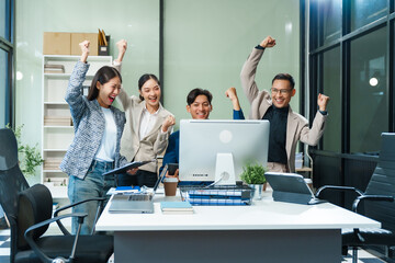 In an office, an Asian team meets at a desk, analyzing financial data on a monitor. They discuss...
