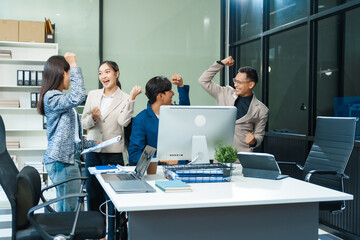 In an office, an Asian team meets at a desk, analyzing financial data on a monitor. They discuss...
