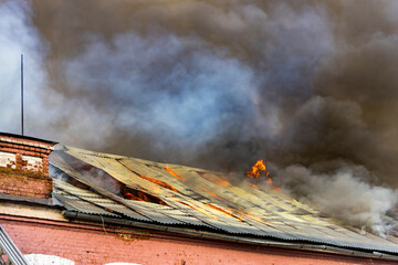 Flames engulf the rooftop as thick smoke billows into the late afternoon sky, highlighting the urgency of the situation in a once peaceful setting.